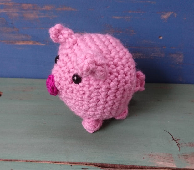 Amigurumi crochet pig pattern - pink crocheted mini pig on blue and green wooden background