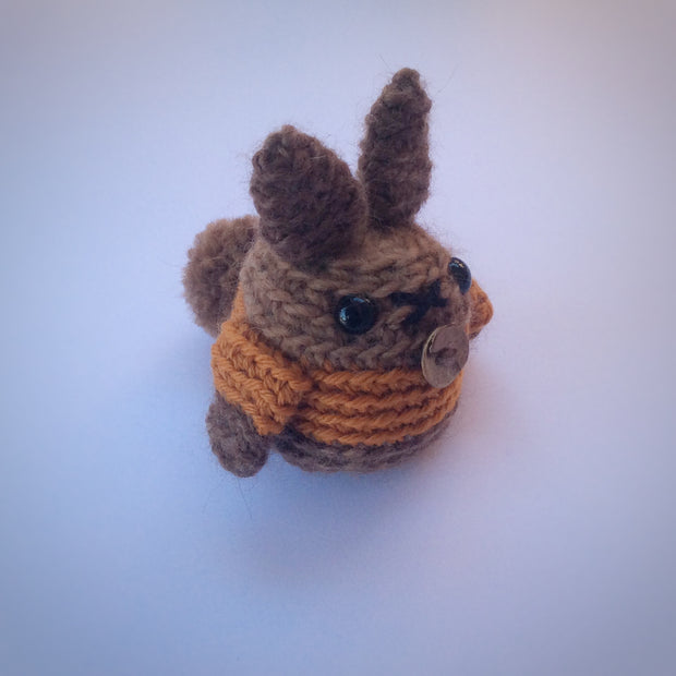 Brown amigurumi bunny made in the round. Wearing an orange jacket and pictured on a white background