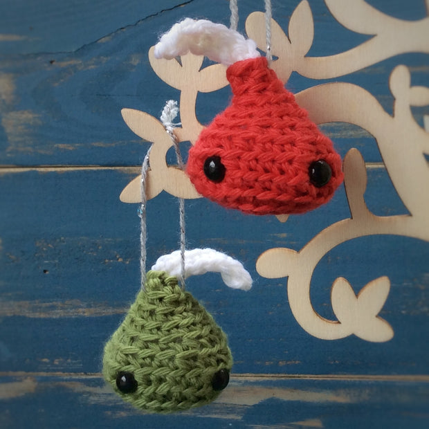 free amigurumi pattern pdf - green and red Chocolate kisses hung on a tree in front of a blue wooden background