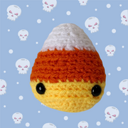 halloween plush - crocheted amigurumi candy corn against a blue white and pink skulls graphic