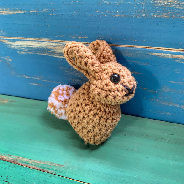 Brown crocheted bunny with brown and white tail on blue and green wooden background